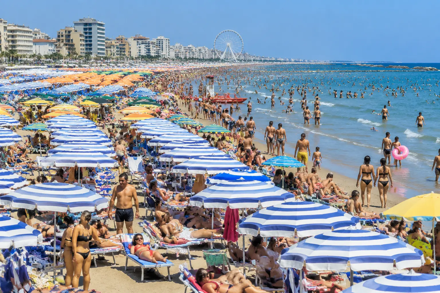 Пляж Римини в августе Переполненный пляж Римини в середине августа: плотные ряды зонтов и отдыхающие у самой кромки Адриатического моря в полдень.